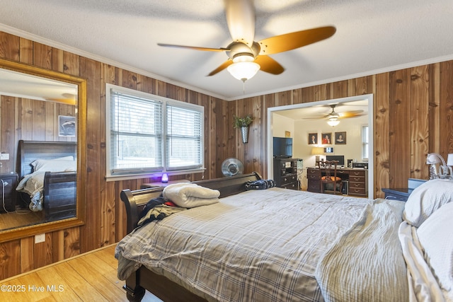 bedroom with ceiling fan, wood walls, crown molding, and a textured ceiling