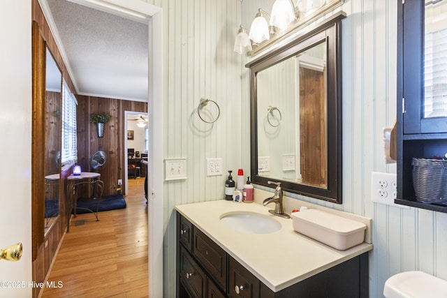 bathroom with crown molding, wood-type flooring, a textured ceiling, vanity, and wood walls