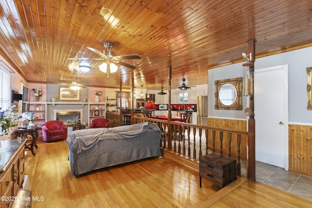 living room with ceiling fan, light hardwood / wood-style flooring, a brick fireplace, and wood ceiling