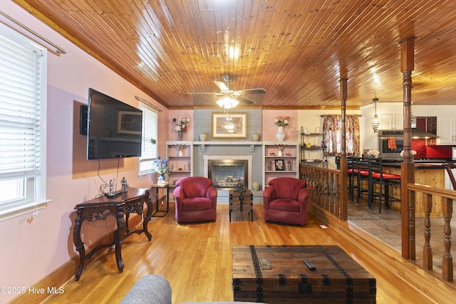 living room with light hardwood / wood-style floors, ornamental molding, ceiling fan, and a fireplace