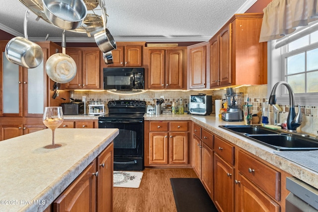 kitchen with sink, a textured ceiling, light hardwood / wood-style flooring, ornamental molding, and black appliances