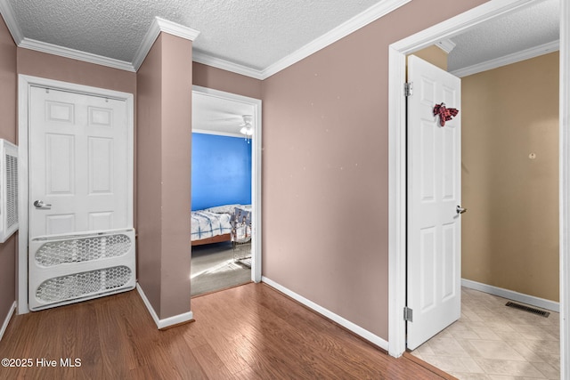 corridor with ornamental molding, light hardwood / wood-style floors, and a textured ceiling