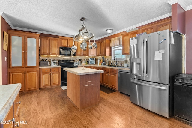 kitchen featuring sink, decorative light fixtures, a center island, light hardwood / wood-style flooring, and black appliances