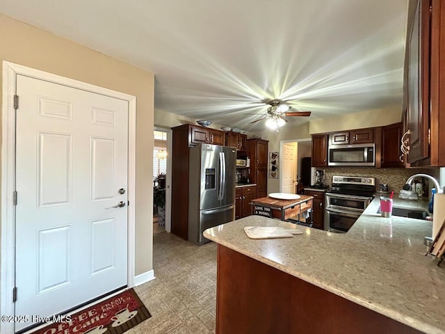 kitchen featuring sink, stainless steel appliances, light stone countertops, decorative backsplash, and kitchen peninsula