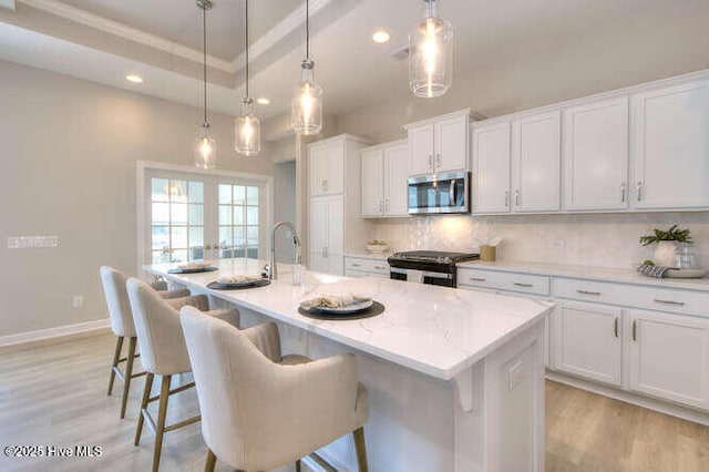 kitchen with appliances with stainless steel finishes, decorative light fixtures, white cabinetry, a kitchen breakfast bar, and a center island with sink