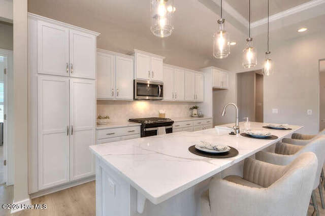 kitchen featuring appliances with stainless steel finishes, pendant lighting, white cabinets, a kitchen bar, and a center island with sink