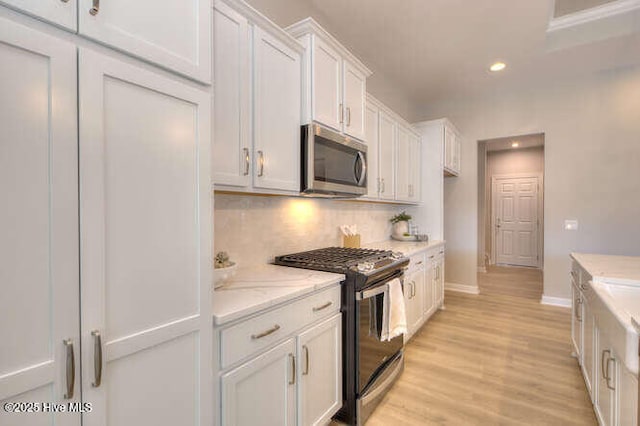 kitchen featuring white cabinetry, light wood-type flooring, appliances with stainless steel finishes, light stone countertops, and decorative backsplash