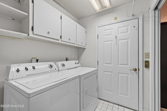 laundry area featuring light tile patterned floors, washing machine and dryer, cabinets, and a textured ceiling