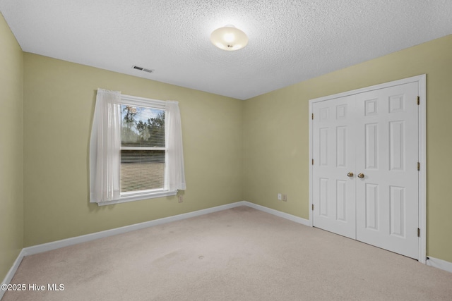 unfurnished bedroom with light colored carpet, a closet, and a textured ceiling