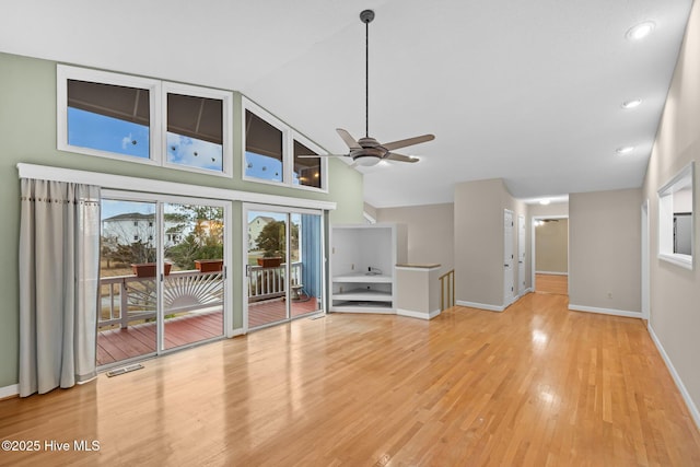 unfurnished living room featuring visible vents, light wood-style flooring, a ceiling fan, high vaulted ceiling, and baseboards