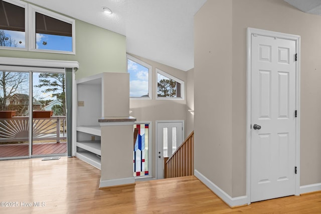 foyer with high vaulted ceiling, a healthy amount of sunlight, and light hardwood / wood-style floors