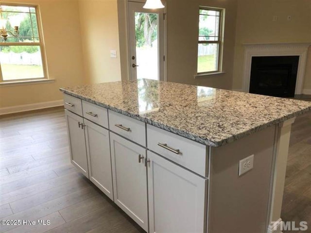 kitchen with light stone countertops, a kitchen island, hardwood / wood-style floors, and white cabinets