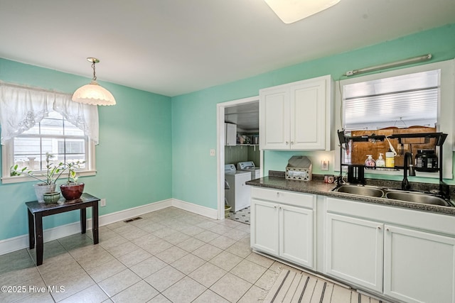 kitchen with white cabinets, hanging light fixtures, sink, and washing machine and clothes dryer