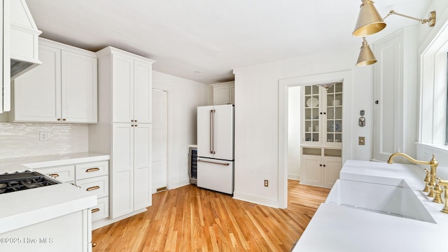 kitchen with hanging light fixtures, light wood-type flooring, white refrigerator, decorative backsplash, and white cabinets