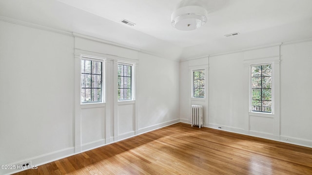 spare room featuring hardwood / wood-style floors, vaulted ceiling, plenty of natural light, and radiator heating unit