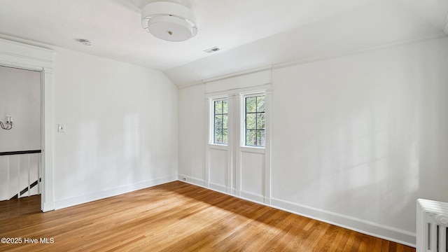 empty room featuring lofted ceiling, radiator heating unit, and wood-type flooring