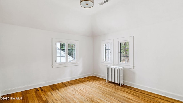 unfurnished room with radiator heating unit, light hardwood / wood-style floors, and vaulted ceiling