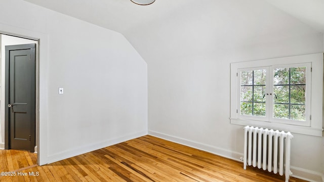 additional living space with radiator heating unit, light hardwood / wood-style floors, and vaulted ceiling