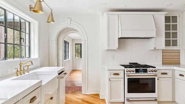 kitchen with range with gas cooktop, white cabinetry, hanging light fixtures, light hardwood / wood-style floors, and backsplash