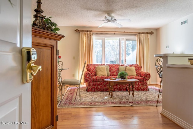 living room with ceiling fan, a textured ceiling, and light hardwood / wood-style floors