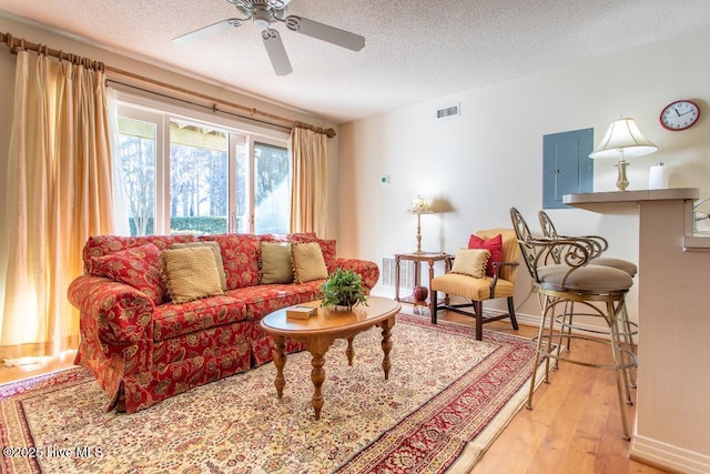 living room with ceiling fan, light hardwood / wood-style flooring, electric panel, and a textured ceiling