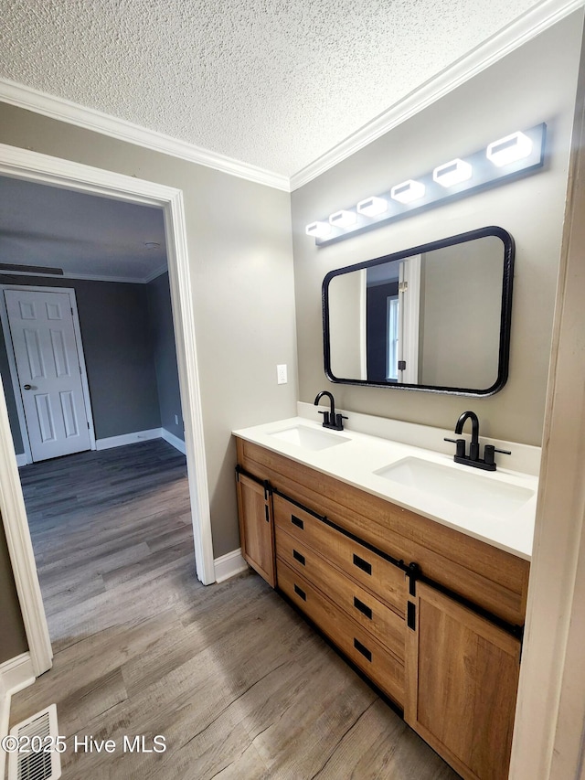 bathroom with vanity, hardwood / wood-style flooring, ornamental molding, and a textured ceiling