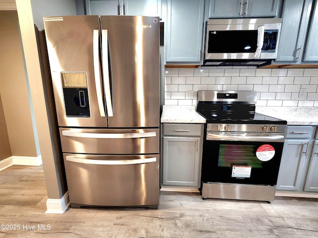 kitchen featuring appliances with stainless steel finishes, gray cabinetry, decorative backsplash, light hardwood / wood-style floors, and light stone countertops