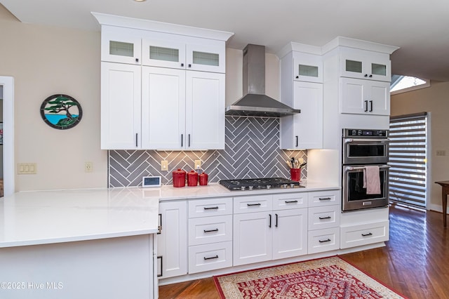 kitchen with dark wood-type flooring, stainless steel appliances, tasteful backsplash, white cabinets, and wall chimney exhaust hood