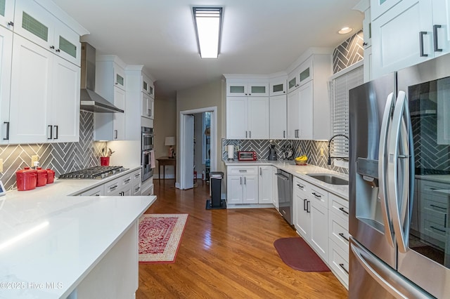 kitchen with sink, hardwood / wood-style flooring, stainless steel appliances, white cabinets, and wall chimney exhaust hood