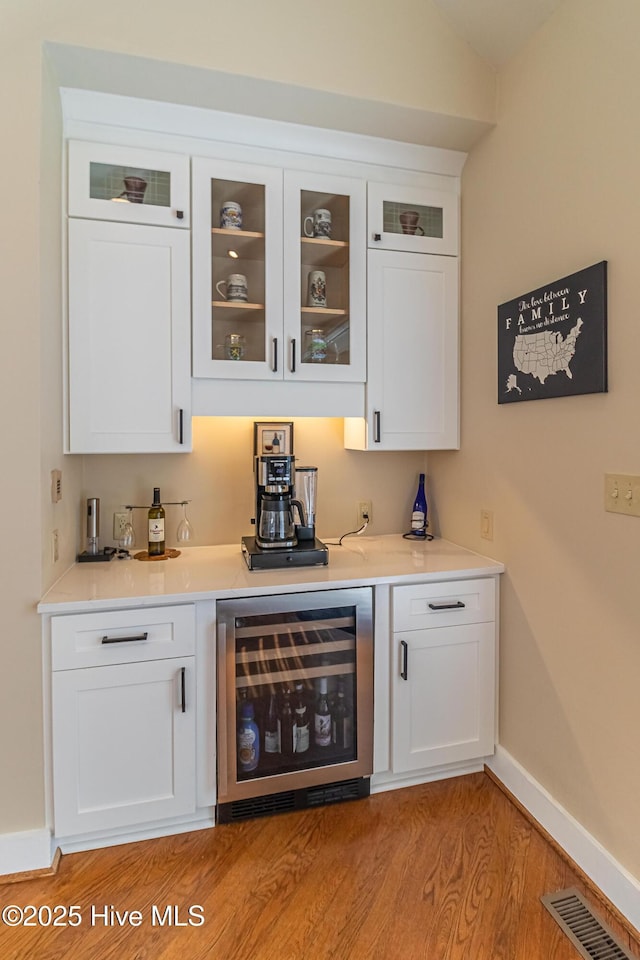 bar featuring wine cooler, lofted ceiling, light wood-type flooring, and white cabinets