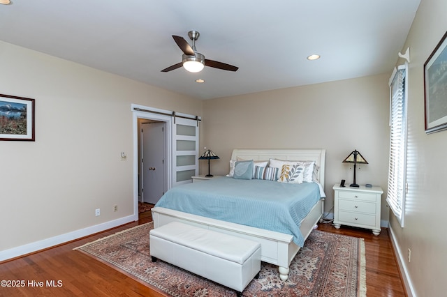 bedroom featuring dark hardwood / wood-style floors, a barn door, and ceiling fan