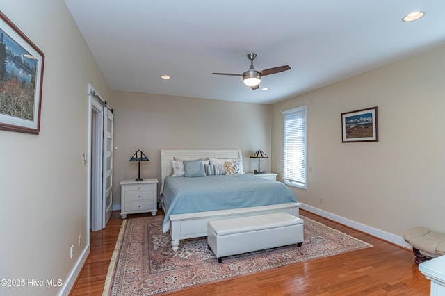 bedroom with ceiling fan, wood-type flooring, and a barn door