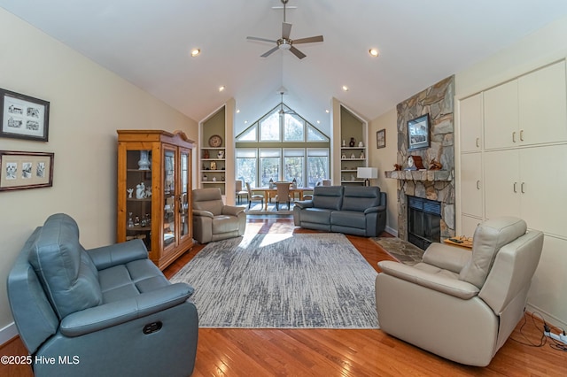 living room featuring built in shelves, a stone fireplace, high vaulted ceiling, and light hardwood / wood-style flooring