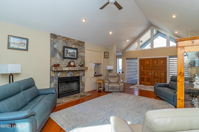 living room with lofted ceiling, a stone fireplace, wood-type flooring, and ceiling fan