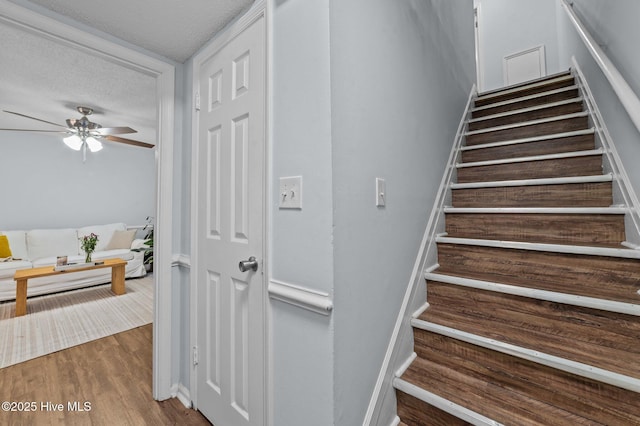 staircase featuring hardwood / wood-style flooring, ceiling fan, and a textured ceiling