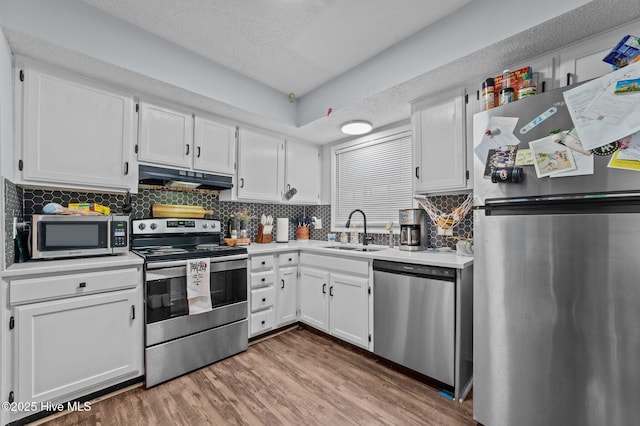 kitchen featuring sink, appliances with stainless steel finishes, backsplash, wood-type flooring, and white cabinets