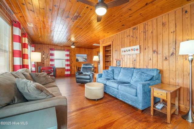 living room featuring wood-type flooring, wooden walls, wooden ceiling, and ceiling fan