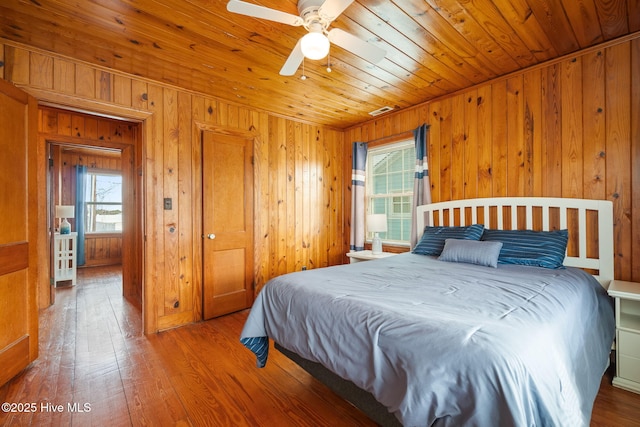 bedroom with multiple windows, hardwood / wood-style floors, ceiling fan, and wood walls