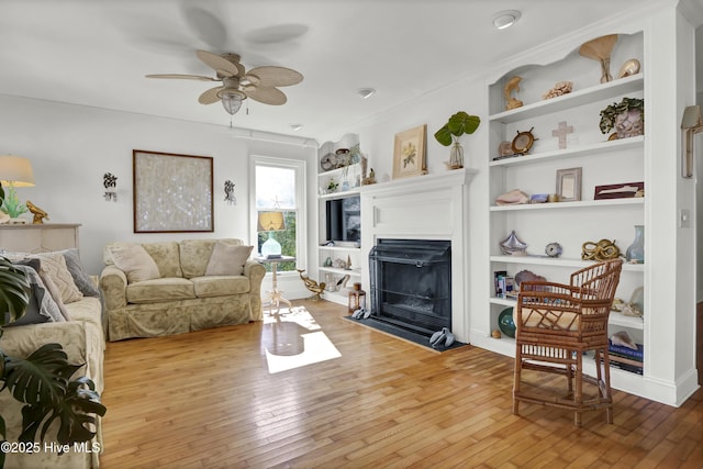 living room featuring crown molding, built in shelves, light hardwood / wood-style flooring, and ceiling fan