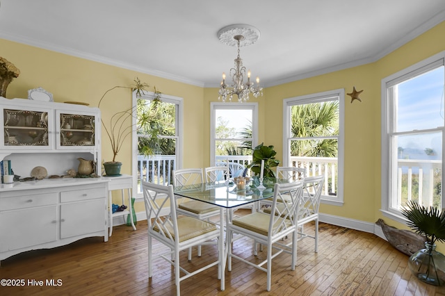 dining area with wood-type flooring, ornamental molding, and an inviting chandelier