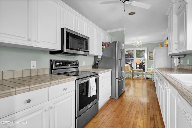 kitchen with ornamental molding, appliances with stainless steel finishes, tile counters, and white cabinets