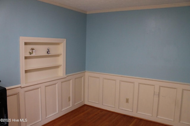 spare room featuring crown molding, built in shelves, and dark wood-type flooring