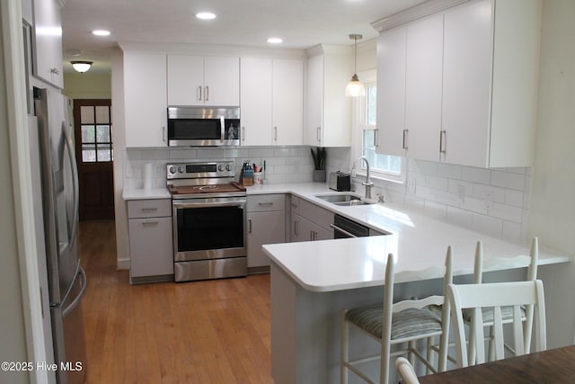 kitchen with sink, decorative light fixtures, appliances with stainless steel finishes, kitchen peninsula, and white cabinets