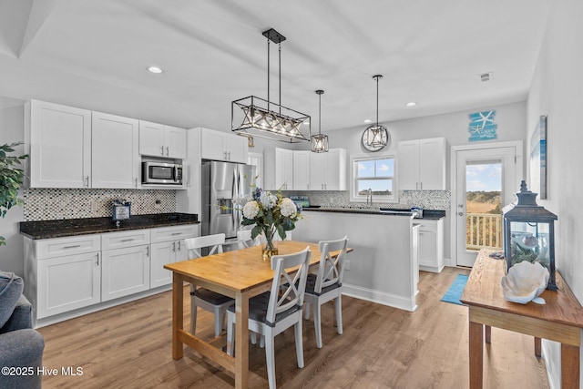 kitchen featuring decorative light fixtures, light wood-type flooring, stainless steel appliances, decorative backsplash, and white cabinets