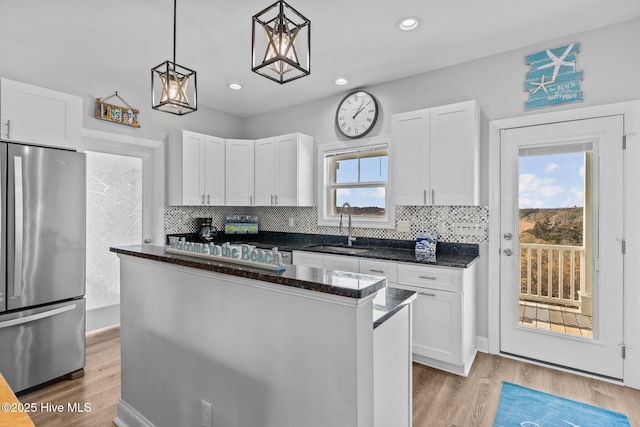 kitchen with hanging light fixtures, sink, stainless steel refrigerator, and white cabinets