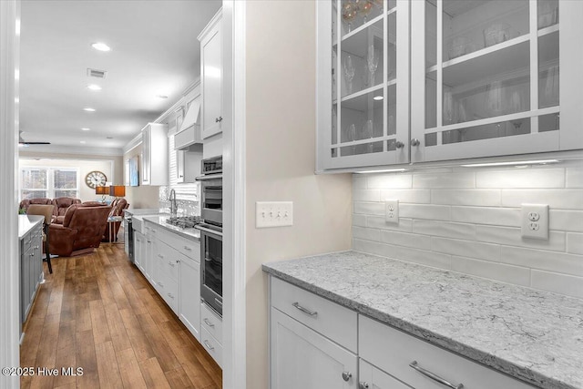 kitchen featuring white cabinetry, tasteful backsplash, stainless steel appliances, light stone countertops, and light hardwood / wood-style floors