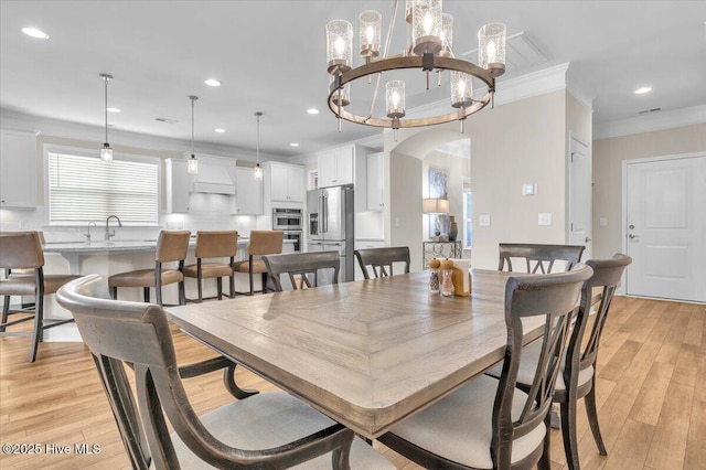 dining area featuring an inviting chandelier, sink, crown molding, and light wood-type flooring