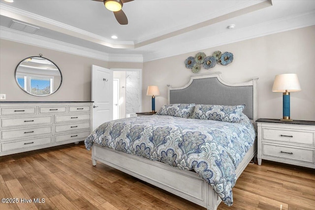 bedroom with crown molding, a tray ceiling, and light hardwood / wood-style flooring