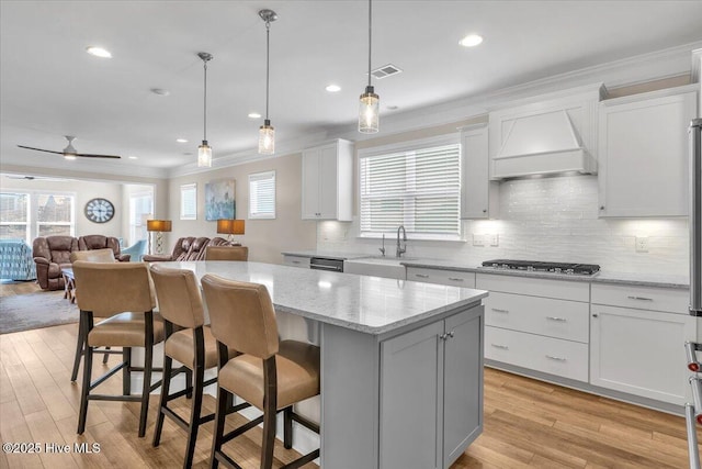 kitchen with white cabinetry, stainless steel appliances, a kitchen breakfast bar, a kitchen island, and custom exhaust hood