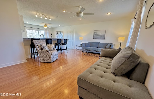 living room featuring ceiling fan, light hardwood / wood-style flooring, rail lighting, and a textured ceiling